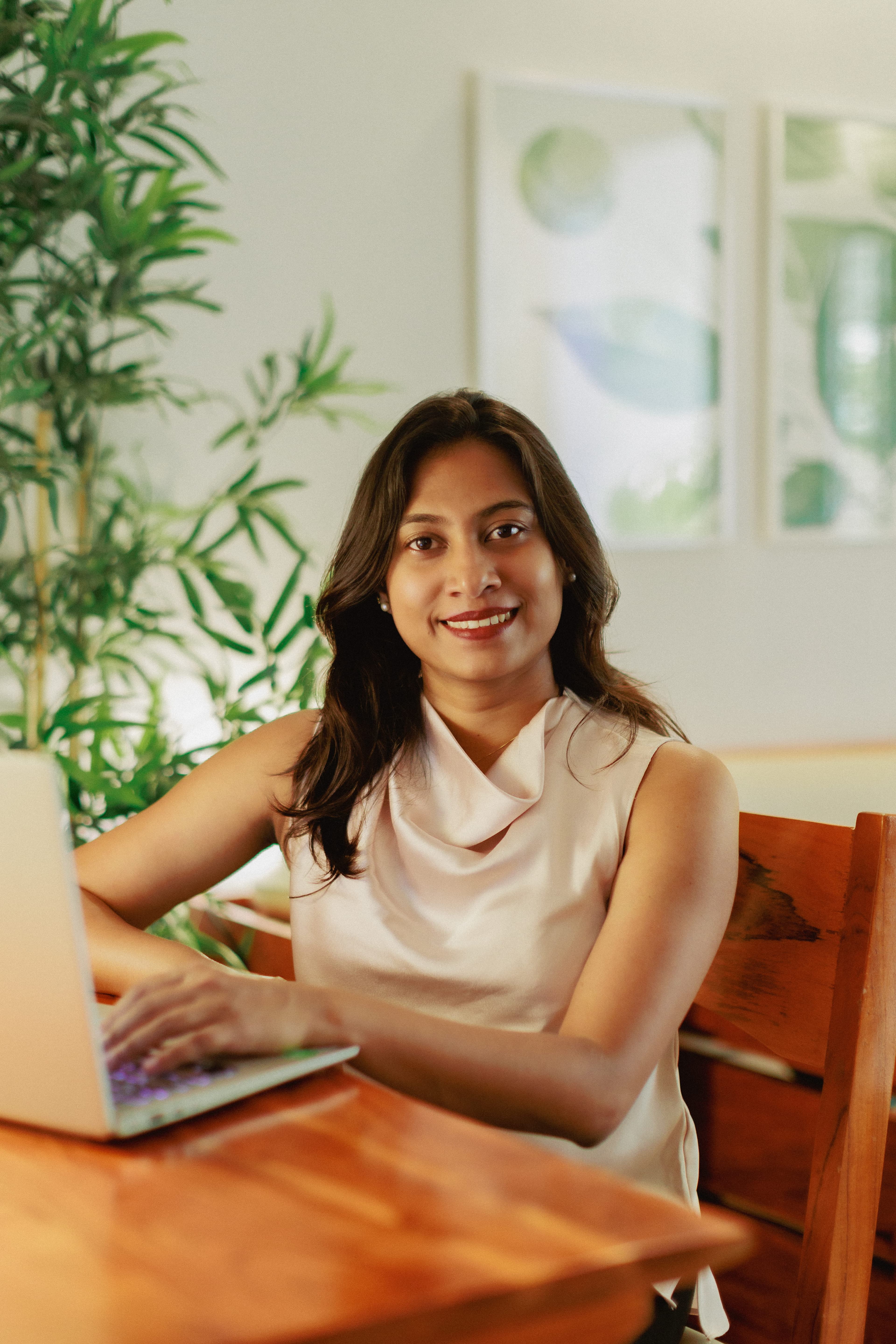 Professional portrait of Neha Johny, founder, at a desk with a laptop in a bright office setting